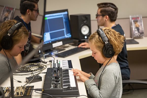 A young girl wears headphones and uses an electic keyboard to compose music