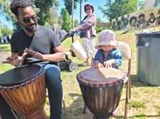 A young child plays the drums with an adult outside at the park.