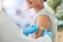 medical employee or healthcare worker applying a band aid to a female patient arm after receiving a vaccine shot.